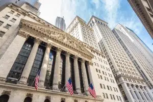 Wall Street, com vista da fachada da Bolsa de Nova York e prédios da cidade ao lado.