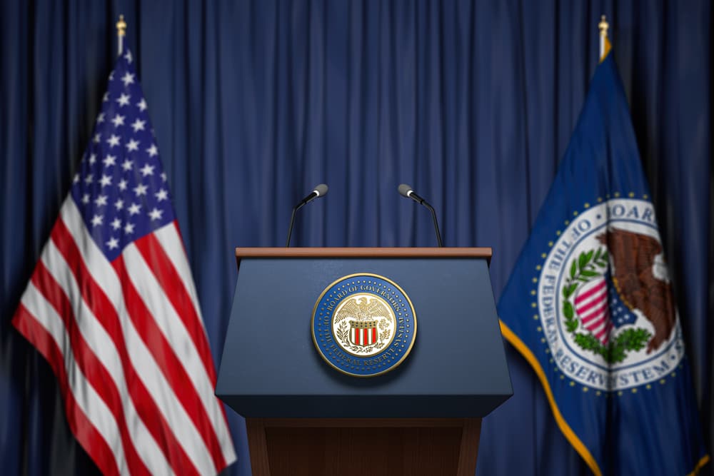 Púlpito para entrevistas do Federal Reserve, com bandeira dos Estados Unidos ao fundo.