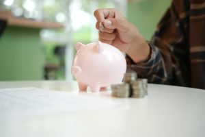 Pessoa depositando moedas em um porquinho, representando a Poupança.