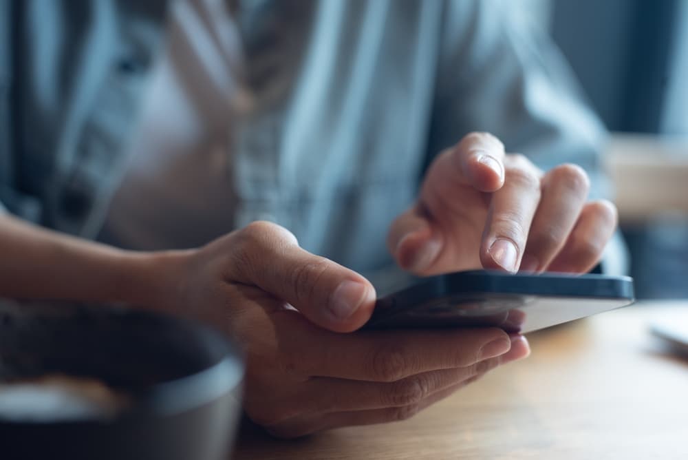 Homem segurando celular, mostrando detalhes da digitação.