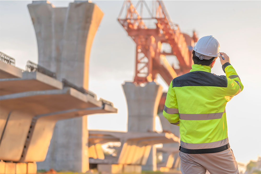 Ponte em construção em segundo plano, com funcionário em primeiro plano.