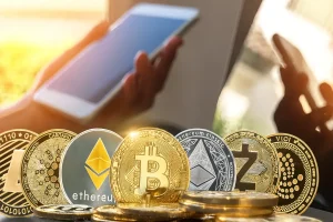moedas de criptoativos sobre teclado com uma mão segurando celular ao fundo em ambiente iluminado.