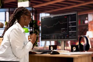 imagem mostra uma mulher investidora sentada e sorrindo olhando a tela do home broker.